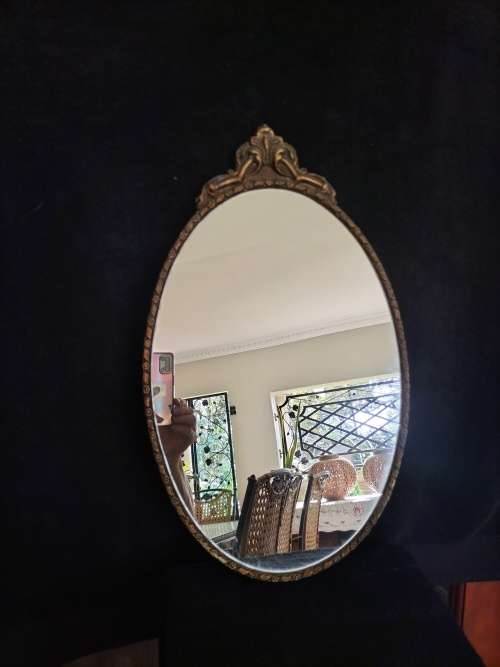 Vintage Gold Oval Mirror With Ornate Detail on top of The Mirror.