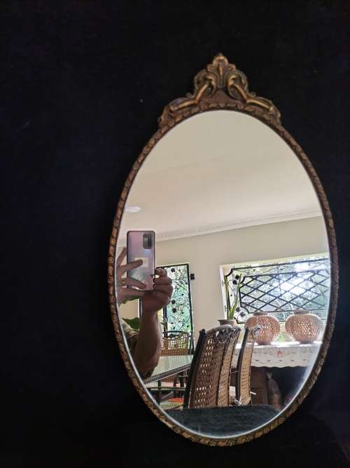Vintage Gold Oval Mirror With Ornate Detail on top of The Mirror.