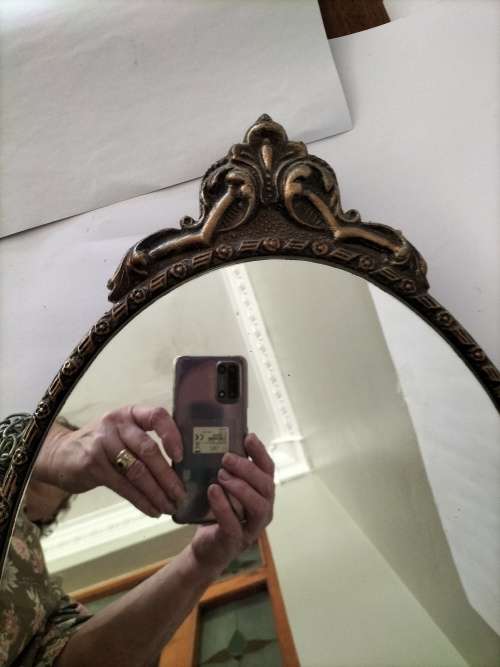 Vintage Gold Oval Mirror With Ornate Detail on top of The Mirror.