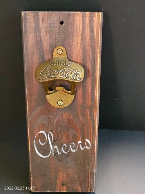 Brass Coca-Cola bottle opener mounted on wood.