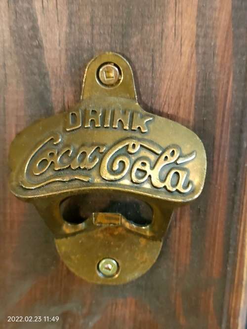 Brass Coca-Cola bottle opener mounted on wood.